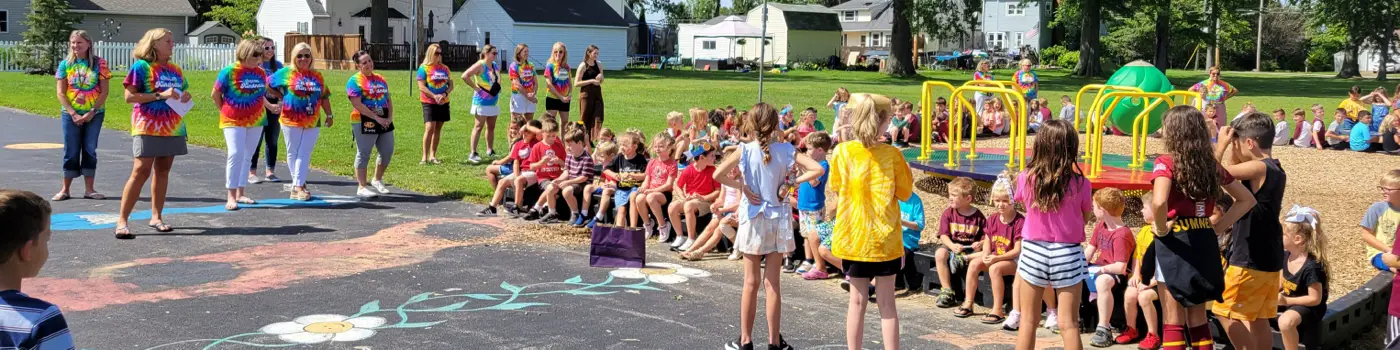 Children and Teachers sitting on playground looking at chalk drawings