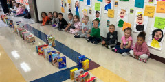 Redwood students sit in school hallway as they watch the domino chain of donated boxed items fall