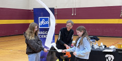 Professor Reggie and two students hold a leaf blower as it blows a stream of paper into the audience