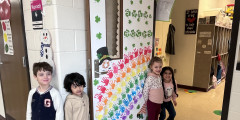 Preschool students smile as they stand next to their decorated classroom door. 