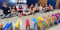 Eastview Kindergarten students smile while sitting in hallway across from domino chain of cereal boxes