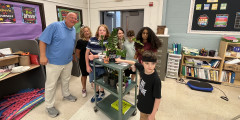 Learwood teachers and staff with students next to wheeled cart with potted plants on top