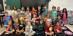 Redwood second grade students sit on carpet while holding up paper dragon puppets