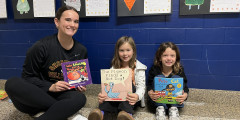 NEHS member and two Eastview students smile while holding books