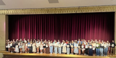 NHS inductees stand on Performing Arts Center stage while holding certificates
