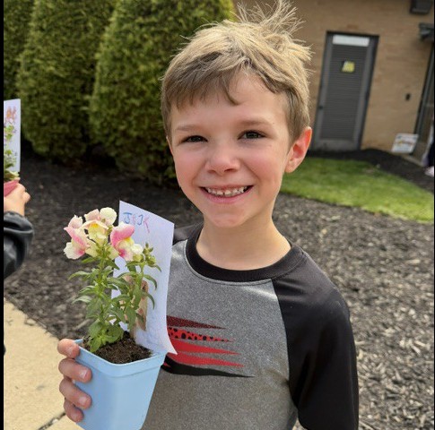 male student holds up potted flower with note of kindness attached