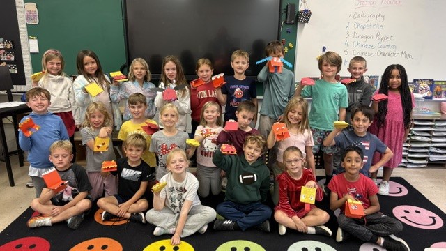 Redwood second graders hold up paper dragon puppets