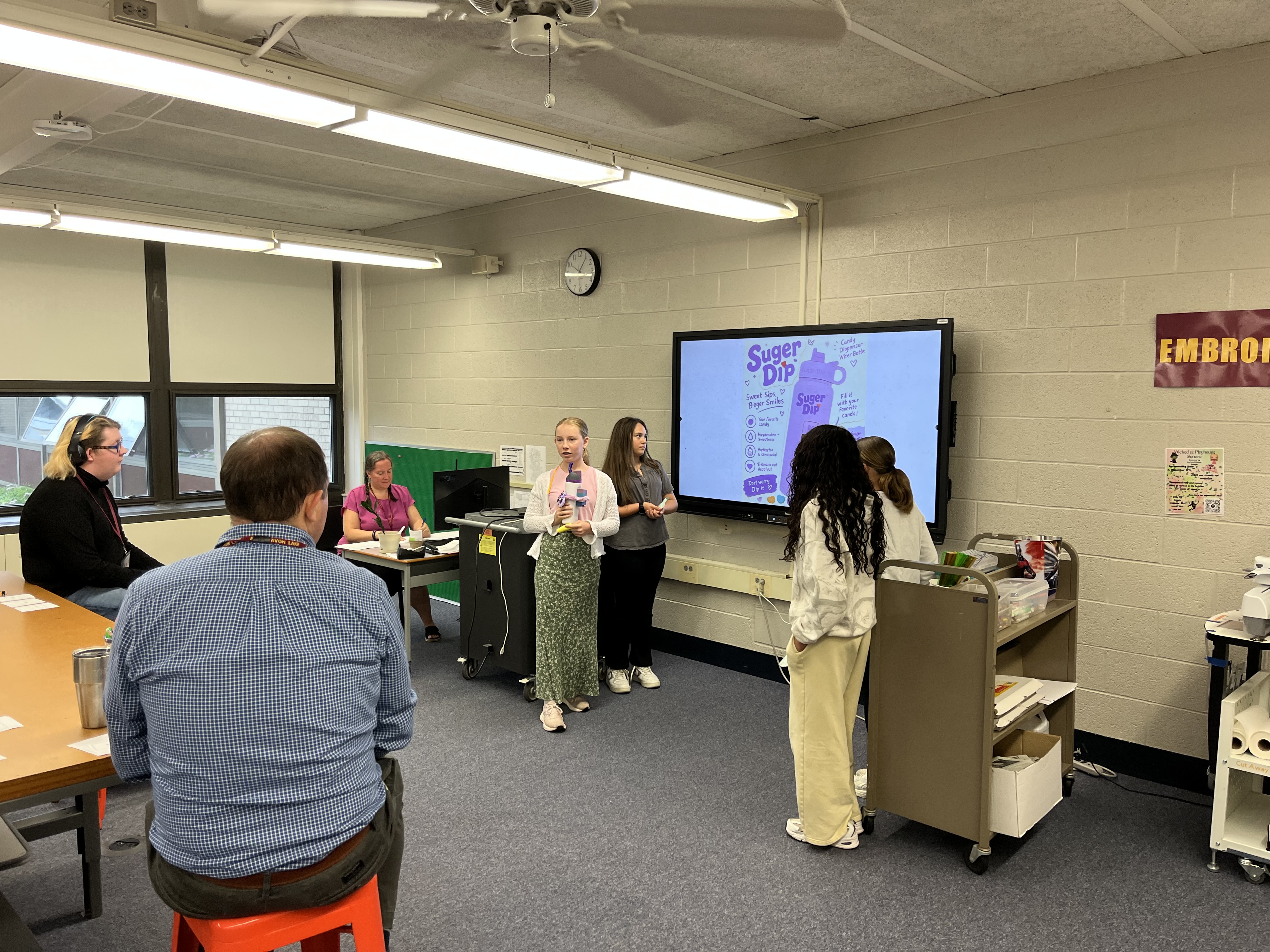 students stand in front of computer screen while presenting about their product