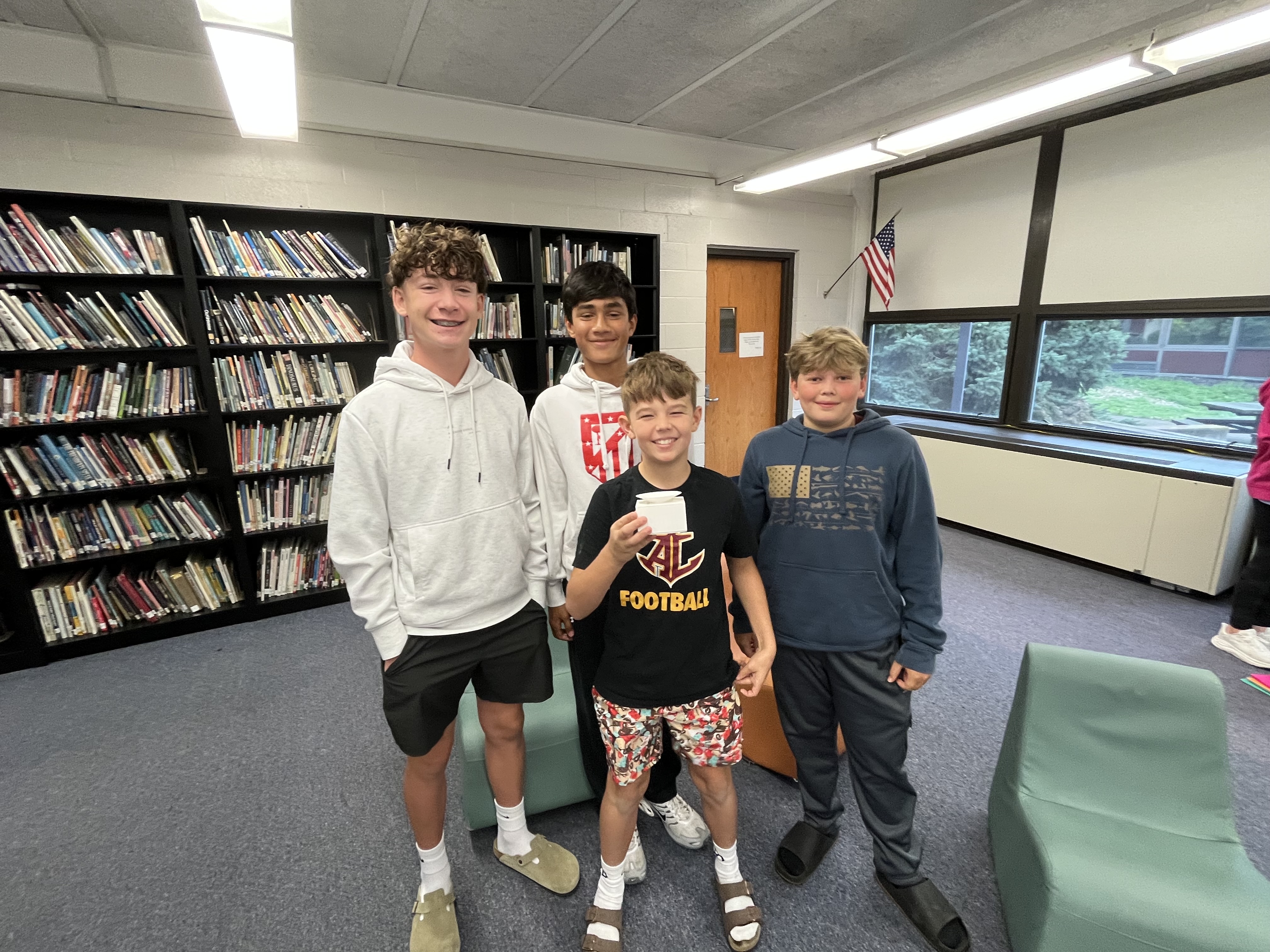 four students stand smiling while holding their prototype