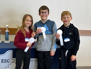Three Redwood fourth grade students hold white ribbons recognizing their third place finish