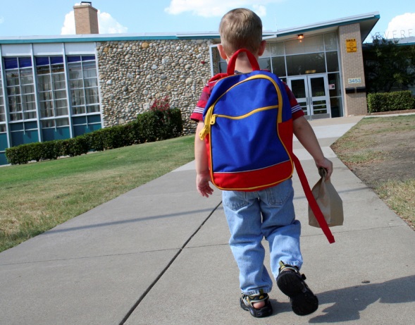 Young boy with backpack walking to school building